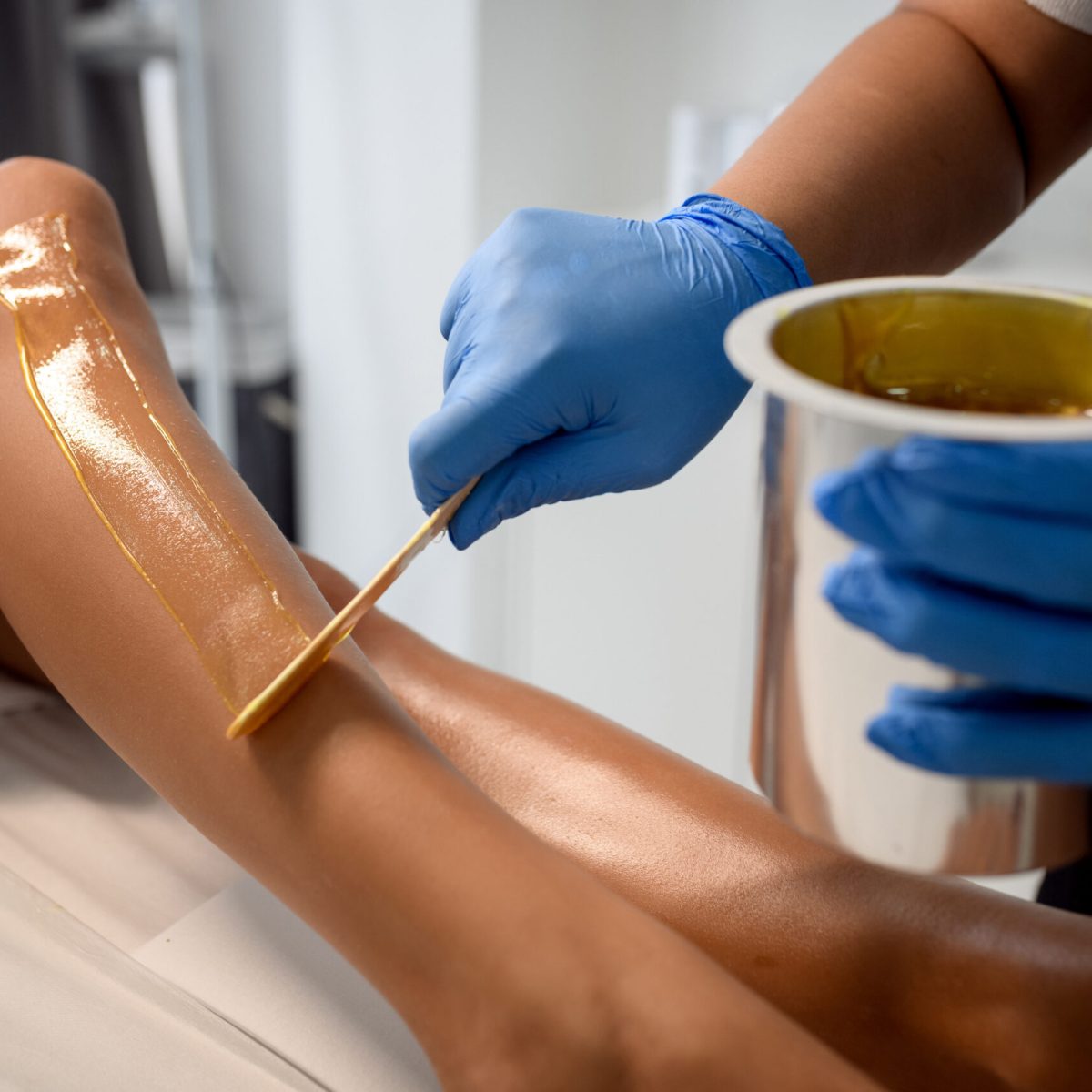 Woman having hair removal procedure on leg with sugaring paste in salon